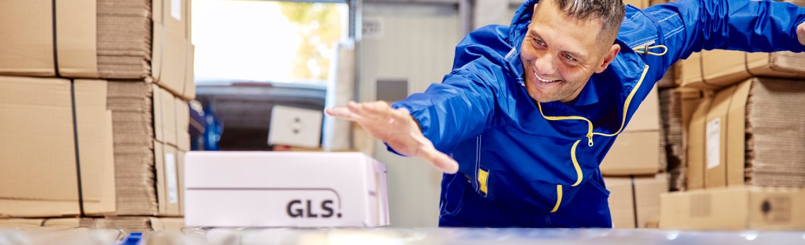 A GLS employee is sliding a parcel on the parcel conveyor belt.