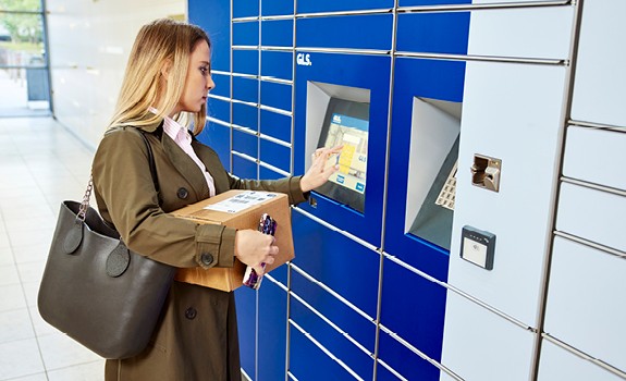 Femme récupérant un colis dans un casier automatique GLS, utilisant l’écran tactile pour entrer ses informations.